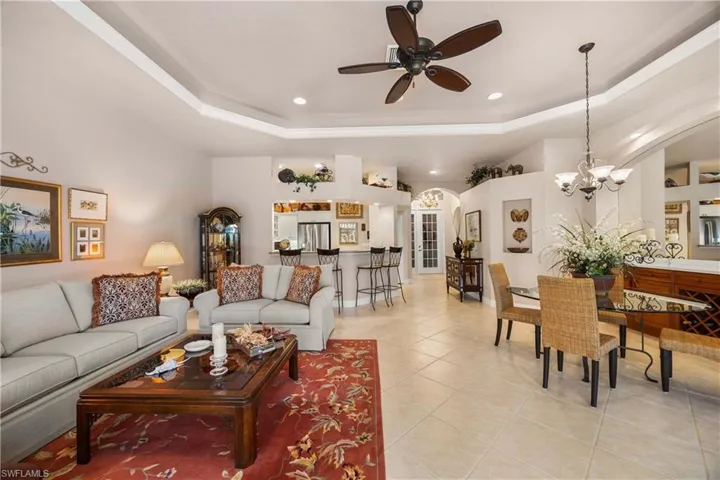 Living area featuring a raised ceiling, arched walkways, a ceiling fan, light tile patterned floors, and recessed lighting