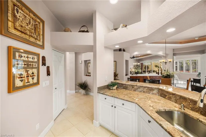 Kitchen featuring light stone counters, pendant lighting, light tile patterned floors, white cabinets, and a chandelier