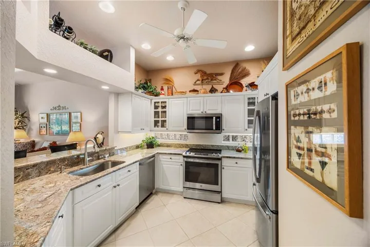 Kitchen with appliances with stainless steel finishes, light stone counters, white cabinetry, light tile patterned floors, and glass insert cabinets