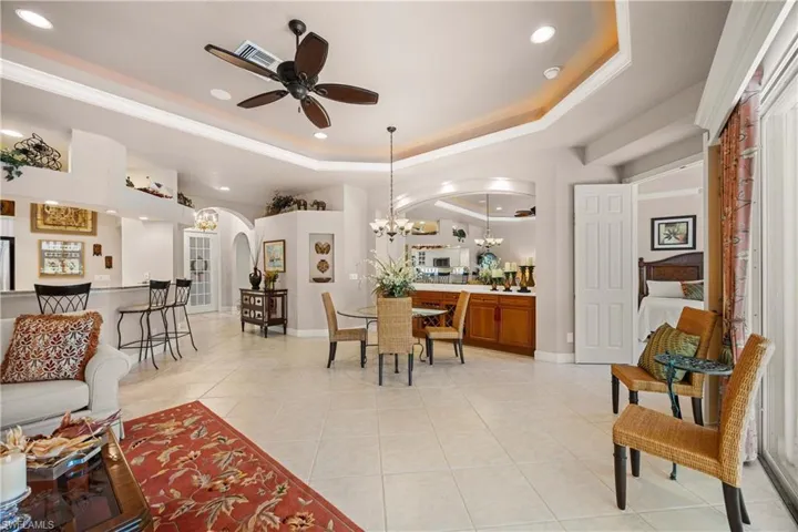 Living room featuring a tray ceiling, light tile patterned floors, a chandelier, recessed lighting, and a ceiling fan