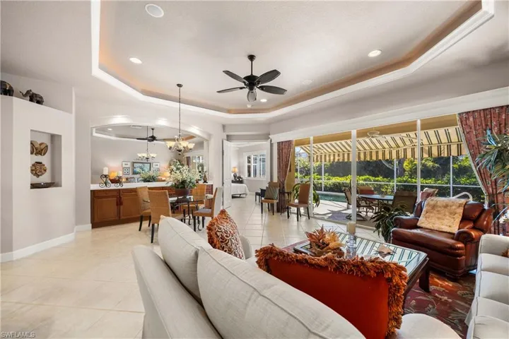Living room featuring a tray ceiling, light tile patterned flooring, ceiling fan, recessed lighting, and a chandelier