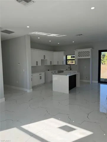 Kitchen with white cabinetry, light stone counters, a center island, recessed lighting, and light marble finish flooring