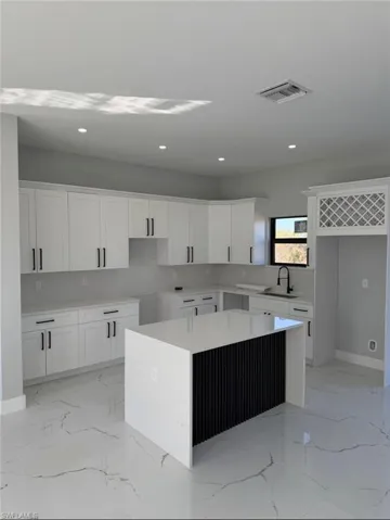 Kitchen with a kitchen island, light stone counters, white cabinetry, recessed lighting, and light marble finish floors