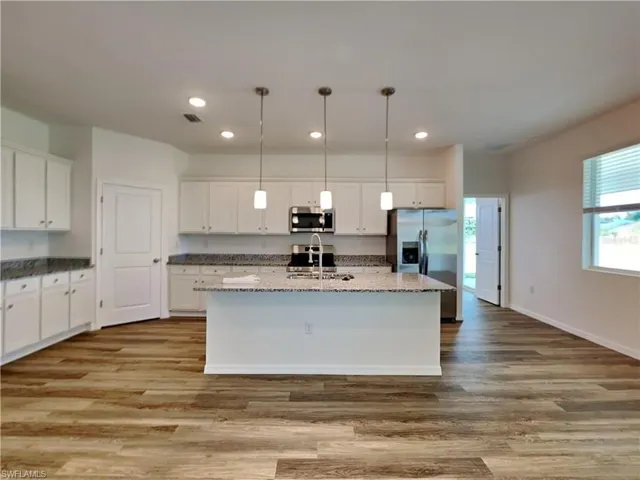 Picture of a previously completed home Kitchen featuring stainless steel appliances, a center island with sink, white cabinets, a sink, and wood finished floors