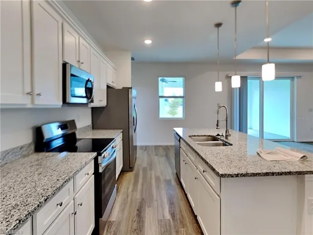 Picture of a previously completed home Kitchen with stainless steel appliances, a sink, light wood-style floors, white cabinets, and a center island with sink