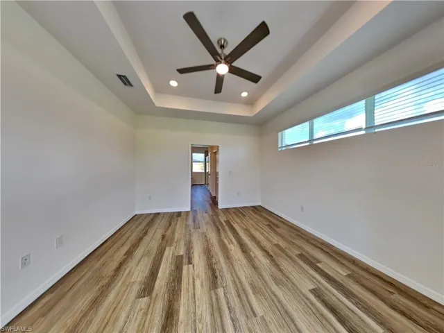 Picture of a previously completed home Spare room featuring wood finished floors, ceiling fan, baseboards, a tray ceiling, and recessed lighting
