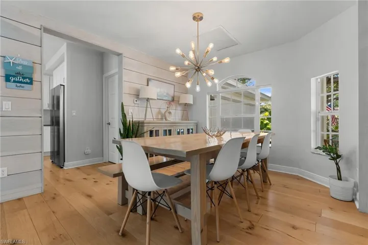 Bright dining space featuring light wood-finish flooring, a contemporary chandelier, a shiplap accent wall, and multiple windows