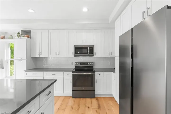 Modern kitchen featuring white shaker cabinetry, stainless steel appliances, dark countertops, a subway tile backsplash, and light wood-finish flooring