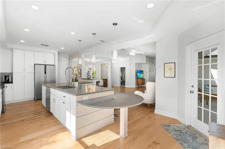 Gourmet kitchen featuring a large central island with integrated seating, stainless steel appliances, abundant white cabinetry, light wood-finish flooring, and recessed ceiling lighting