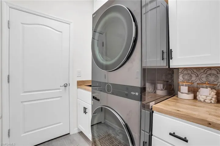 Laundry area featuring cabinets, stacked washer / drying machine, and light hardwood / wood-style floors