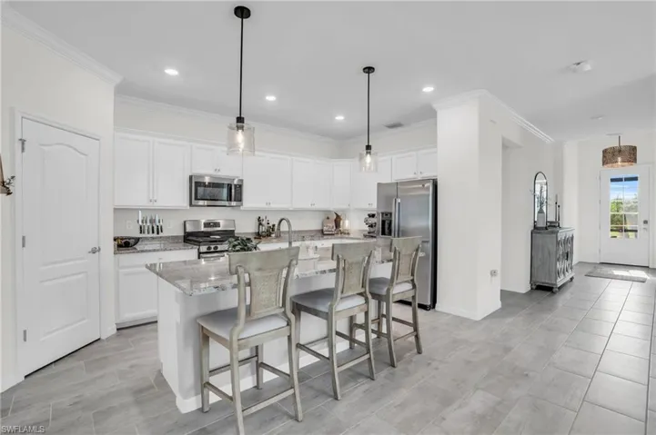 Kitchen featuring appliances with stainless steel finishes, white cabinetry, light stone counters, and an island with sink