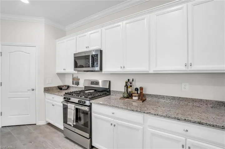 Kitchen featuring white cabinets, light stone countertops, stainless steel appliances, and crown molding
