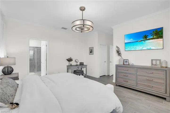 Bedroom featuring a chandelier, ensuite bathroom, crown molding, and light hardwood / wood-style flooring