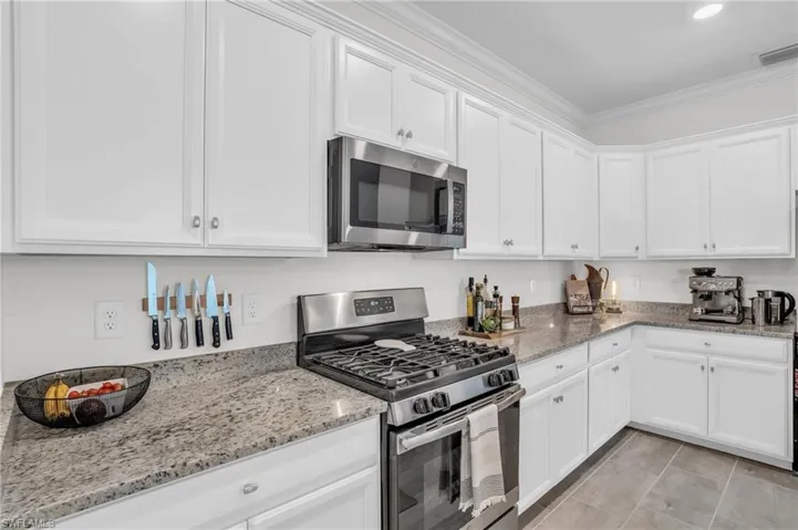 Kitchen featuring ornamental molding, white cabinetry, stainless steel appliances, and light stone countertops