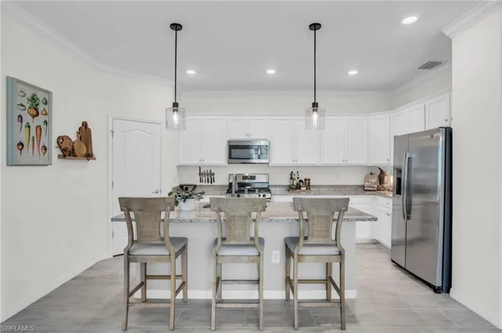 Kitchen featuring a kitchen island with sink, crown molding, light stone countertops, hanging light fixtures, and appliances with stainless steel finishes
