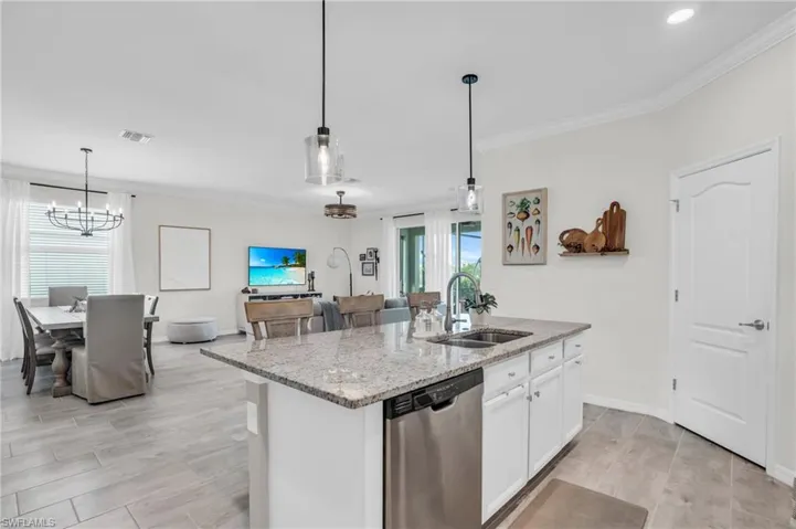 Kitchen featuring light stone countertops, an island with sink, stainless steel dishwasher, sink, and white cabinets