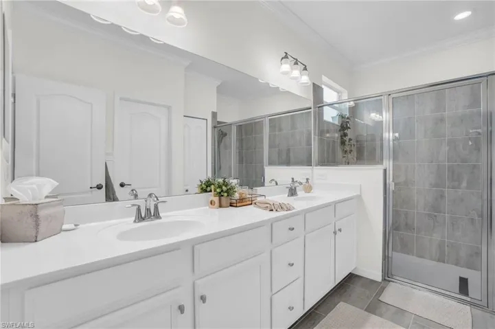 Bathroom featuring tile patterned flooring, a shower with door, ornamental molding, and vanity