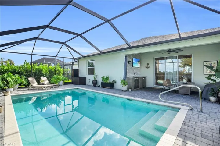View of pool with glass enclosure, ceiling fan, and a patio