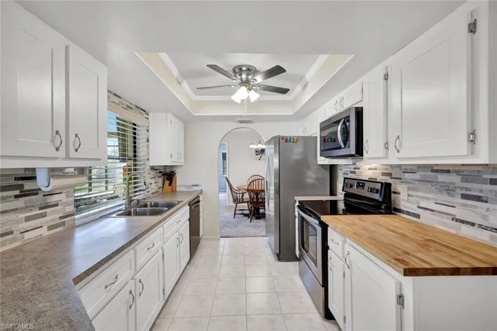 Kitchen with tasteful backsplash, arched walkways, stainless steel appliances, and white cabinets