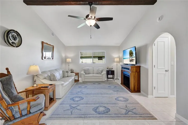 Living area featuring lofted ceiling, a ceiling fan, arched walkways, and light tile patterned floors