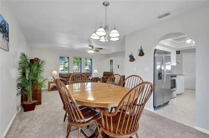 Dining area with a ceiling fan, arched walkways, light carpet, and a chandelier