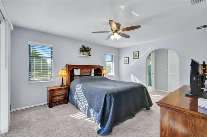 Bedroom featuring light colored carpet, arched walkways, and ceiling fan