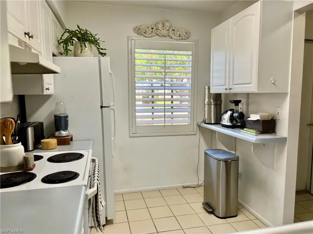 Kitchen with white electric stove, white cabinets, light countertops, and light tile patterned flooring