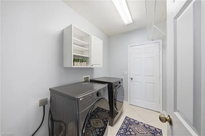 Dedicated laundry area featuring tile flooring, overhead fluorescent lighting, white cabinetry, and a white six-panel door