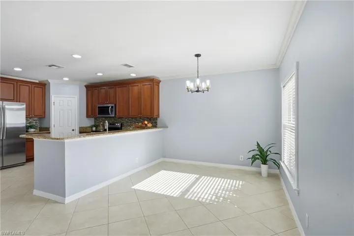 Open-concept kitchen and dining area featuring warm wood cabinetry, stainless steel appliances, a granite-finish countertop, and a tiled backsplash