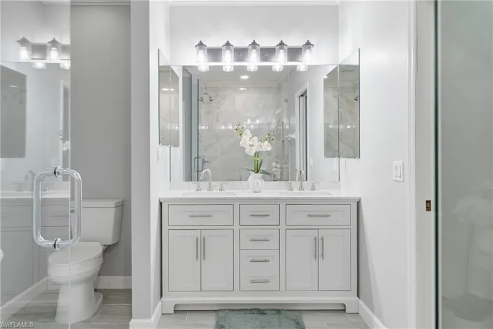 Dual vanity with white cabinetry and integrated sinks, complemented by a large mirror and multi-bulb fixture