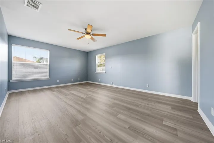 Spacious room featuring light blue walls, wood-finish flooring, and white baseboards