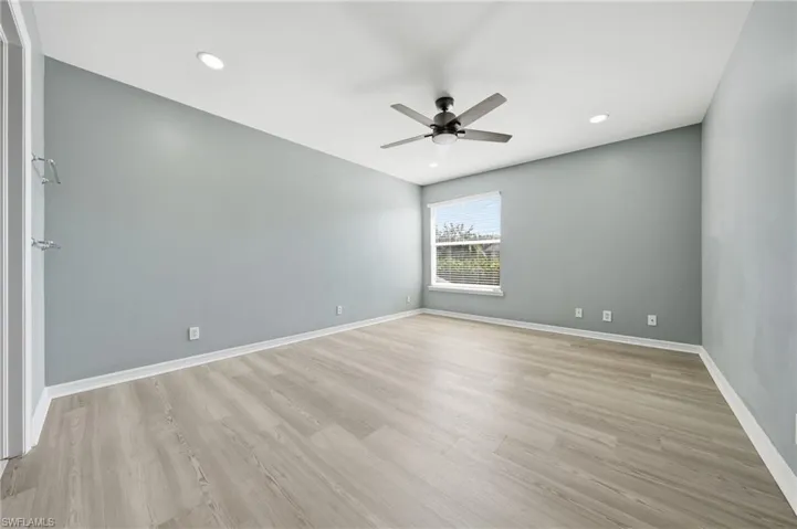 Spacious room featuring light wood-finish flooring, a ceiling fan with integrated lighting, recessed lighting, and a window with blinds