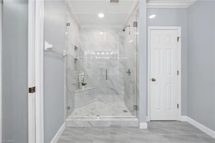 Frameless glass shower enclosure featuring marble-look tile walls, a built-in corner bench, and dual recessed shelves