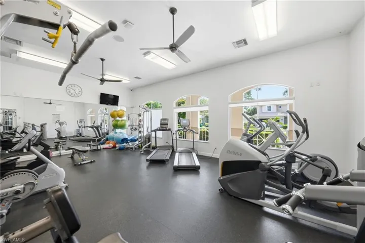 Fitness center featuring ample natural light from arched windows, dark rubber flooring, and multiple ceiling fans