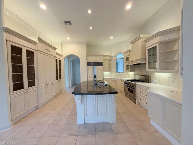 Gourmet kitchen featuring a large central island with dark countertop, extensive cabinetry with glass and solid fronts, stainless steel range, and tile flooring