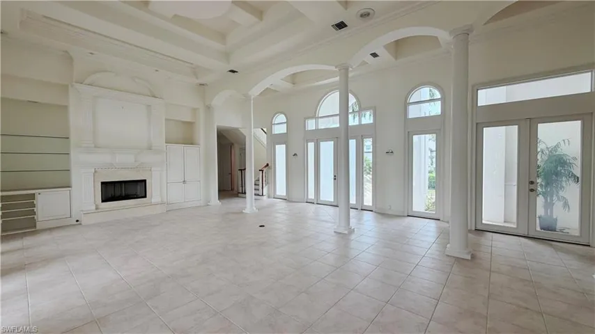 Spacious interior featuring a coffered ceiling, floor-to-ceiling windows, built-in shelving, a fireplace, and column details