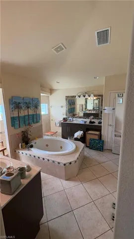 Spacious bathroom featuring a built-in jetted tub with tiled surround, large vanity with dual sinks, extensive counter space, and tile flooring