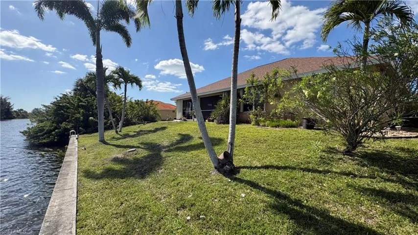 Waterfront property featuring a concrete seawall, mature palm trees, manicured lawn, and lush landscaping