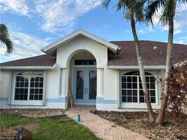 Property exterior featuring a textured stucco finish with light blue accents, a brown shingle roof, and a stamped concrete walkway