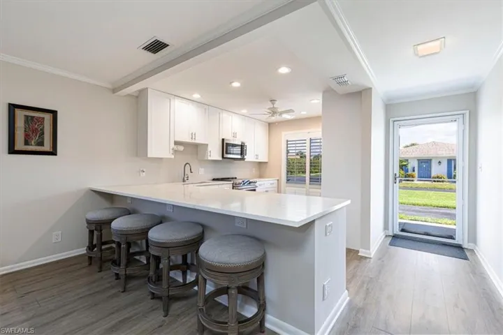 Kitchen featuring light wood-style flooring, a peninsula, a breakfast bar, crown molding, and white cabinetry