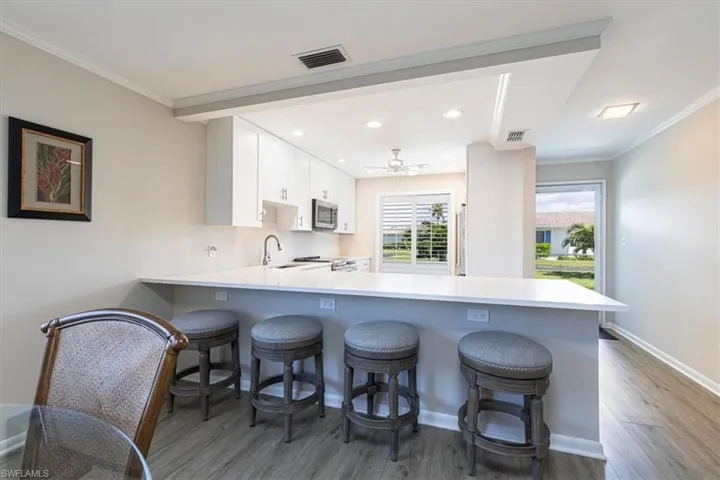 Kitchen with a expansive peninsula, a kitchen breakfast bar, crown molding, light wood-style floors, and white cabinets