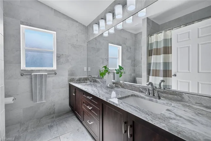 Bathroom featuring tile walls, double vanity, a shower with shower curtain, plenty of natural light, and vaulted ceiling
