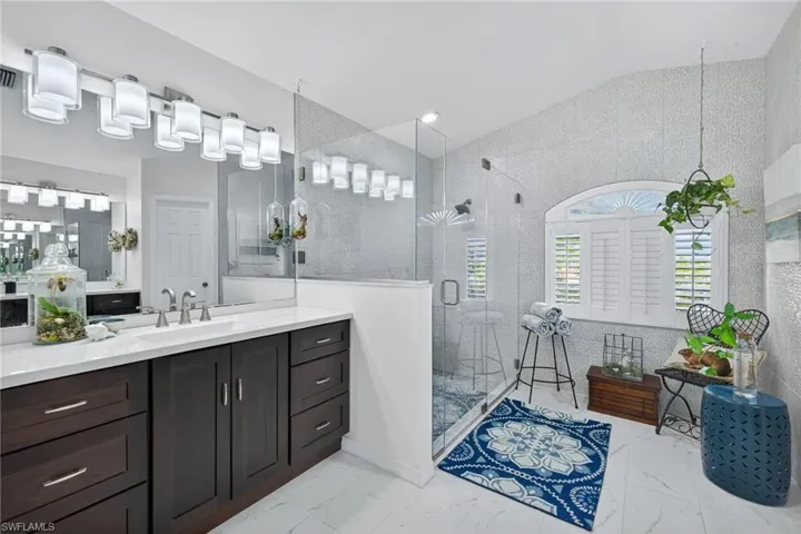 Bathroom featuring vanity, a shower stall, lofted ceiling, and light marble finish flooring