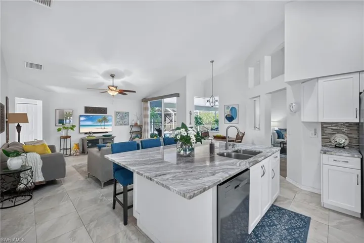 Kitchen with open floor plan, lofted ceiling, light stone countertops, dishwasher, and a breakfast bar area