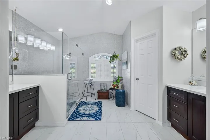 Bathroom featuring vanity, a shower stall, vaulted ceiling, and light marble finish floors