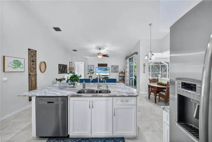 Kitchen with stainless steel appliances, white cabinetry, an island with sink, light stone countertops, and decorative light fixtures