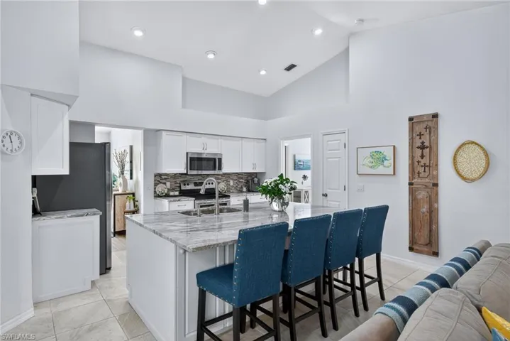 Kitchen with light stone counters, a breakfast bar, white cabinetry, stainless steel appliances, and a kitchen island with sink