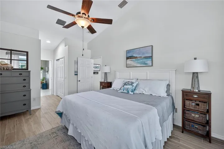 Bedroom featuring wood tiled floors, a ceiling fan, a closet, ensuite bath, and vaulted ceiling