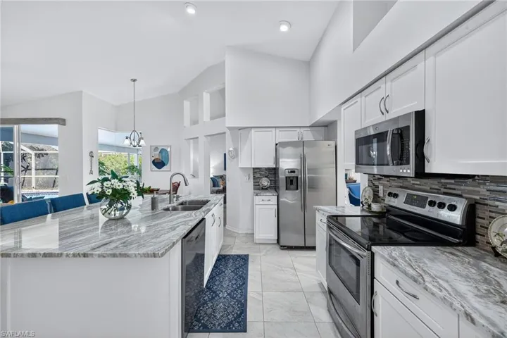 Kitchen featuring stainless steel appliances, light stone counters, tasteful backsplash, white cabinetry, and lofted ceiling