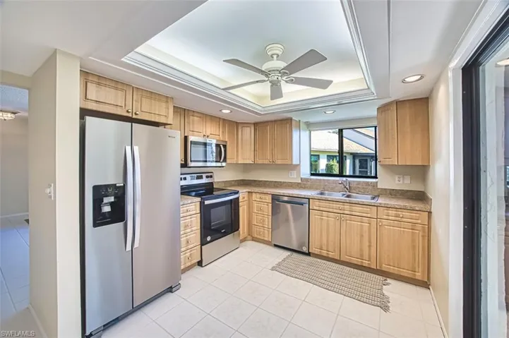 Kitchen featuring appliances with stainless steel finishes, a raised ceiling, a ceiling fan, light tile patterned flooring, and light countertops